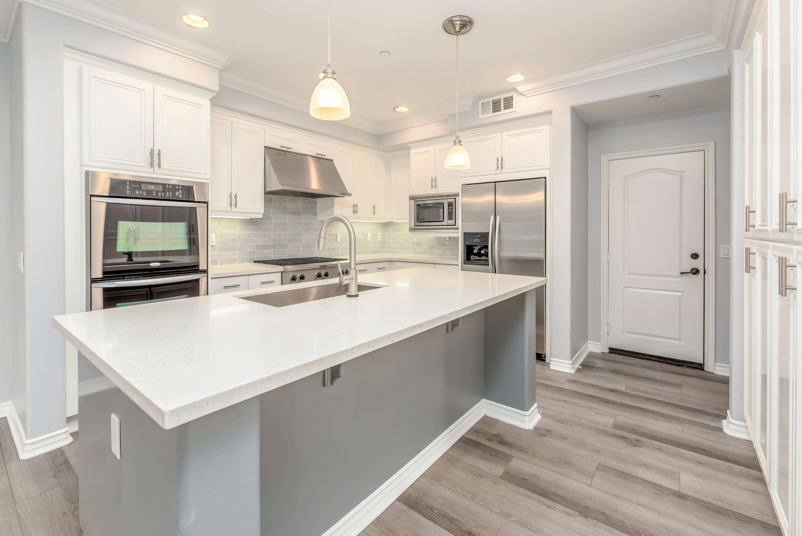 Modern white kitchen renovation with stainless steel appliances, quartz countertop island, and light grey wood flooring in Edmonton home.