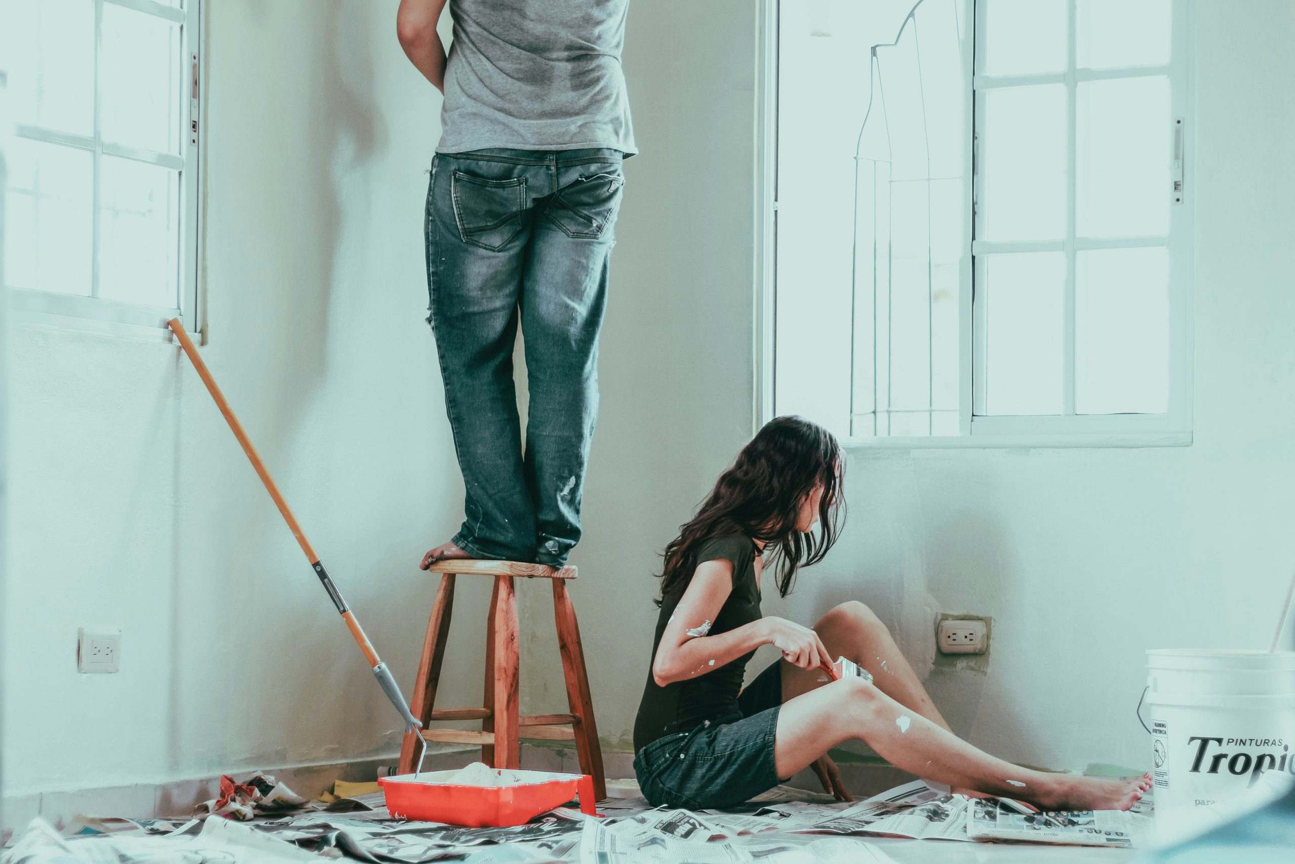Couple painting and renovating a room together with paint tools and drop sheets around, illustrating a DIY home renovation scene