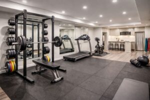 Finished basement home gym with weight rack, treadmill, rubber flooring, and modern lighting in an Edmonton home